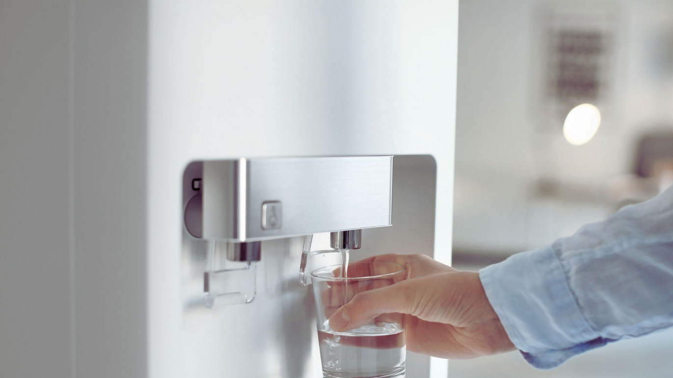 Hand füllt ein Glas mit Wasser aus einem modernen Wasserspender