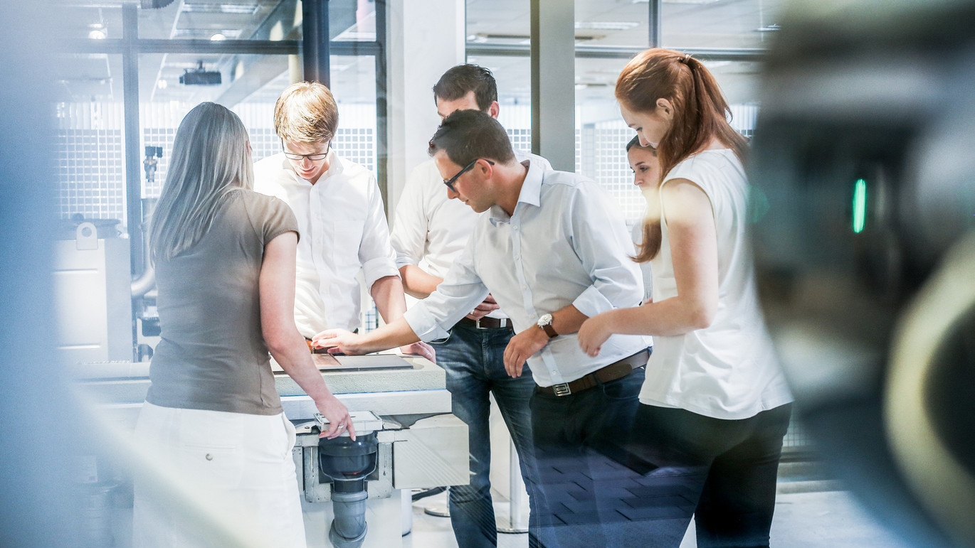 Gruppe von fünf Personen in heller Kleidung arbeitet konzentriert an einem Tisch in einem modernen Büro oder Labor, fördert Teamarbeit und Zusammenarbeit