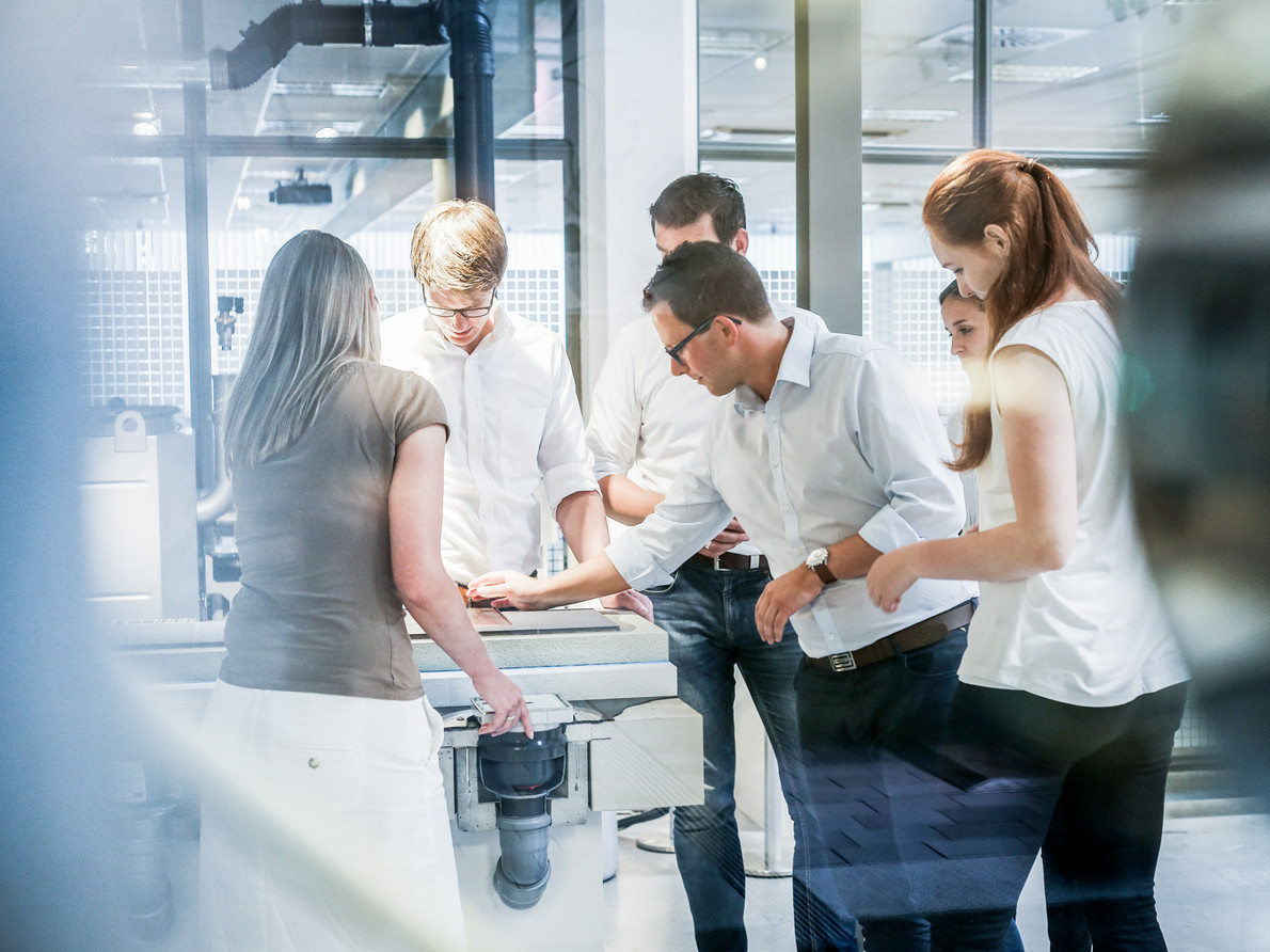 Gruppe von fünf Personen in heller Kleidung arbeitet konzentriert an einem Tisch in einem modernen Büro oder Labor, fördert Teamarbeit und Zusammenarbeit